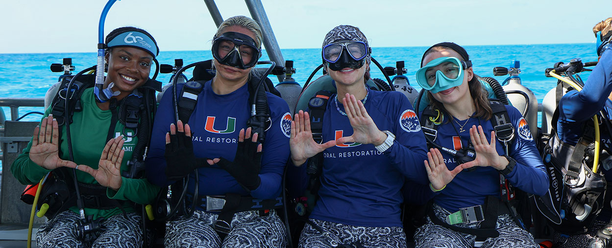 Image shows divers throwing the "U" with their hands as they sit on the bench and prepare to enter the water